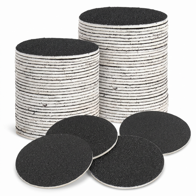 Stacked black sandpaper foot file refill discs on white background